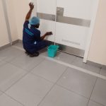 Cleaning staff member in protective workwear wiping the lower section of a large white door beside a small bucket