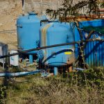 Blue industrial water-treatment tanks, pipes, pumps, and filtration equipment installed outdoors at a fenced facility